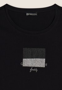 Camiseta de algodón negra con un gráfico rectangular texturizado en negro y plateado que presenta el texto "GLAMOUR" y el logo "freddy" en la parte inferior.