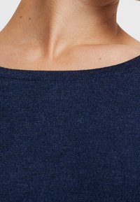 Top in maglina blu navy con ampia scollatura, texture a coste e tessuto morbido, mostrato dalle spalle alla scollatura, senza decorazioni.