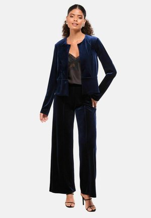 Sjöblå sammet kostymset bestående av en figursydd kavaj med rund halsringning och vida byxor. Outfiten har en mjuk yta och subtil lyster.