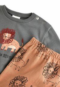 Grå baby sweatshirt med grafisk rød løve og teksten "Vær Modig", parret med ferskenfarvede bukser med sort løvemønster og elastisk talje. 