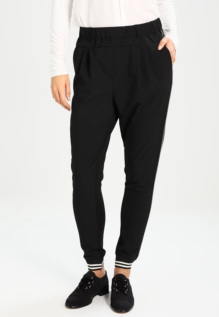Les pantalons de jogging noirs sont dotés d'une taille élastique, de poches latérales et d'accents rayés au niveau des poignets. Fabriqués en matière douce et extensible.