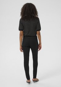 Black fitted pants paired with a short-sleeve black and white striped top. Fabric appears smooth with a slight stretch. Minimalistic design.
