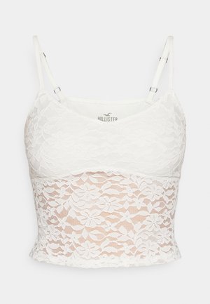 Balta nėriniuota marškinėlių viršutinė su reguliuojamomis petnešėlėmis, gėlių nėrinių raštu ir prigludusia siluetu, su tvirtu pamušalu.