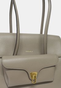 Sac à main en cuir gris avec un design structuré, deux poignées, un rabat à l'avant et un détail de fermoir doré. Logo embossé à l'avant.