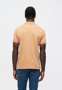 Rövid ujjú, világos barna színű pamut poloing bordázott gallérral és mandzsettával, finom logóval a nyakkivágás közelében.