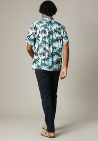 Korte mouwen, lichtblauw knoopshirt met zwart palmbomenpatroon, gecombineerd met donkere broeken en beige instappers.