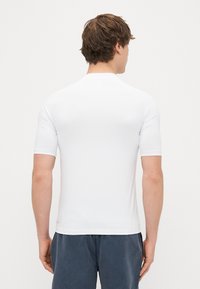 Biała, krótko rękawowa koszula z gładkiego materiału, o dopasowanym kroju, z okrągłym dekoltem i bez widocznych wzorów ani akcentów.