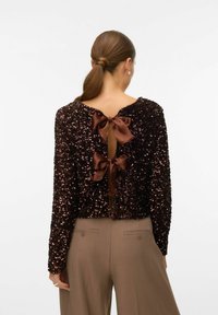 Melns sequin tops ar apaļu izgriezumu, garām piedurknēm un aizmugurējo atvērumu, kas fiksēts ar divām brūnām satīna lentītēm.