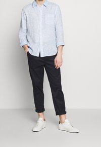 Jasnoniebieska koszula z długim rękawem w wzór paisley, rękawy podwinięte do łokci, w połączeniu z ciemnymi spodniami i białymi sneakersami.