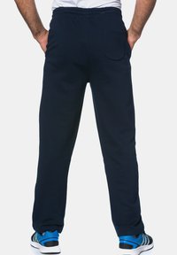 Navy blue sweatpants with an elastic waistband and a back pocket, displayed from the rear, paired with athletic shoes featuring blue accents.
