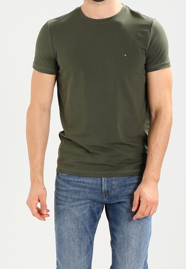 T-shirt verde oliva con colletto a girocollo realizzato in morbido cotone, con maniche corte e un piccolo logo ricamato sul petto. Abbinato a jeans blu.