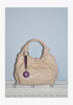 Beež, läikiv sünteetiline käekott kogutud disainiga, sõlmitud käepide ja eemaldatav lilla sädelev ripats. Ümar kuju.