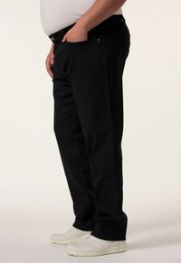 Pantalones de mezclilla negra con corte recto, que cuentan con un cierre delantero de botón y cremallera, bolsillos laterales, y se combinan con zapatillas blancas.