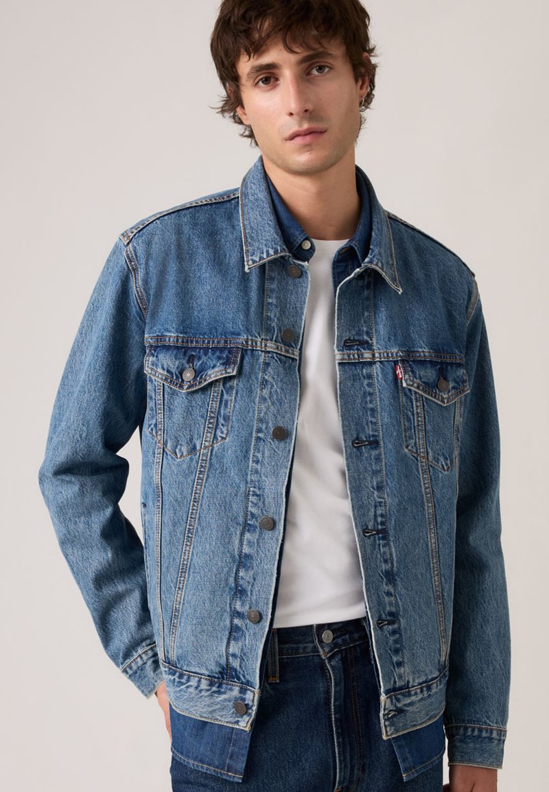 Τζιν μπουφάν σε ανοιχτό μπλε με κλασική γραμμή, εμπρόσθιους κουμπιά, δύο τσέπες στο στήθος και αντιθετική ραφή. Φορεμένο πάνω από λευκό T-shirt.