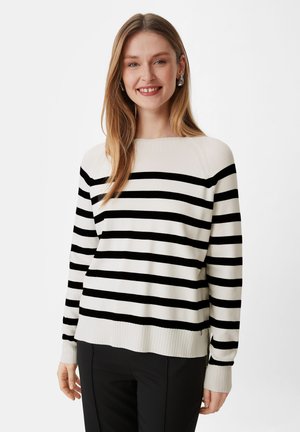 Gestreifter Pullover in Schwarz-Weiß mit einem gerippten Halsausschnitt und Bündchen. Lockere Passform und weiche Textur, kombiniert mit schwarzen Hosen.