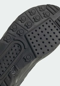 Black footwear sole with varying textures, including smooth and pebbled sections. Features patterned grips and ventilation holes.