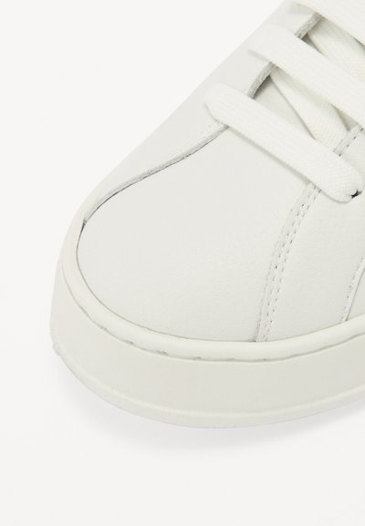 Hvit sneaker med en glatt lær-overdel, rund tå, flat gummisåle og hvite snøringer, med synlige sømmer langs kantene.
