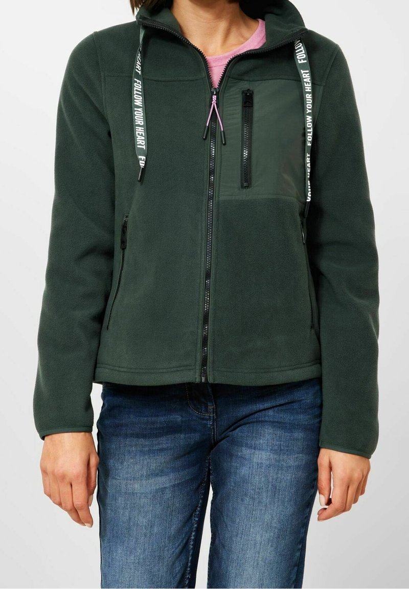 Ciemnozielona polarowa kurtka z wysokim kołnierzem, zamkiem na piersi i regulowanymi sznurrkami, ozdobiona wzorem tekstowym. Slim fit.