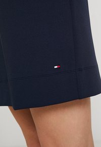 Granatowe szorty z teksturowanej tkaniny, z małym czerwono-białoniebieskim logo na końcu. Czysty design i prosty krój.