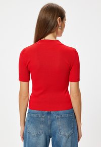 Top rosso a righe con maniche corte, colletto, design aderente e lunghezza cropped, abbinato a jeans in denim blu a vita alta.