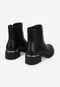 Botas de cuero negras hasta el tobillo con punta redondeada, cremallera en la parte posterior y un acento dorado en el tacón, con un diseño de tacón cuadrado.