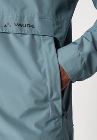 Ljust blå vattentät jacka med ficka och logodetalj. Slät textur, justerbar ärm och minimalistisk design. Miljövänligt material.