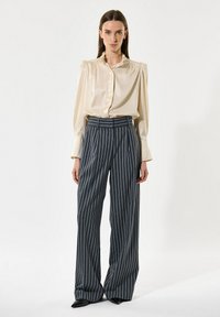 Bež satenasta bluzica z nabranim ovratnikom, v kombinaciji z mornarsko modrimi hlačami širokega kroja s črtami. Ozek kroj, gladka tekstura in prilagojen dizajn.