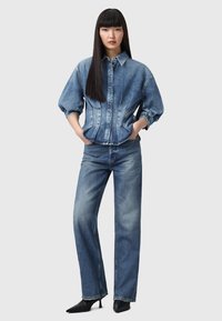 Giacca in denim con silhouette strutturata, maniche a palloncino e zip frontale, abbinata a jeans in denim a gamba dritta in un lavaggio medio.