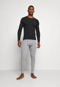Schwarz langärmliges Oberteil kombiniert mit hellgrauen, eng anliegenden Hosen. Beide haben eine glatte Textur und ein minimalistisches Design, die Hosen verfügen über gerippte Bündchen.