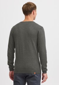 Pull à manches longues pour homme, en gris foncé, texture tricotée, col rond, ourlet et poignets côtelés, avec un petit patch en cuir au dos.