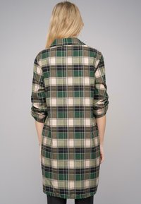 Vestito a quadretti verde e beige con colletto, maniche arrotolate a tre quarti e taglio dritto. La texture del tessuto appare liscia e leggera.