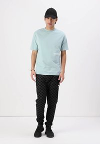 Svetlo modra kratka majica s kratkimi rokavi z majhnim belim logotipom na prsih, v kombinaciji z črnimi houndstooth joggerji in črnimi športnimi copati.