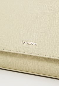 Billetera de cuero beige de Calvin Klein con una superficie texturizada, que presenta un logo plateado en la parte frontal y sutiles detalles de costura.