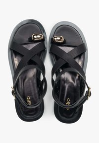 Zwarte sandalen met kruisbanden, voorzien van een bovenwerk van glad leer, een glanzend gouden accent, een gevoerde binnenzool en een flexibele rubberen zool.