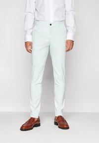 Světlé modré kalhoty na míru z hladké tkaniny, s knoflíkovým zapínáním a slim fit střihem, spárované s hnědými společenskými botami.