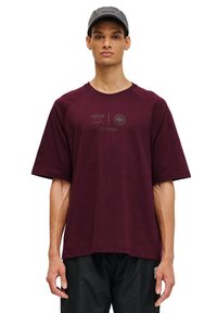 Mörkröd t-shirt med kort ärm och rund halsringning, med tryckta logotyper och text framtill, samt en avslappnad passform. Bärs med svarta byxor.