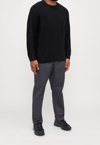 Pull en tricot noir, pantalon gris avec poches latérales, et baskets noires. La tenue présente une coupe décontractée et un tissu texturé.