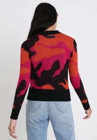 Maglione multicolore con un motivo di camouflage nero, arancione e rosa, bordo a coste sulle maniche e sull'orlo, realizzato in un morbido materiale a maglia.
