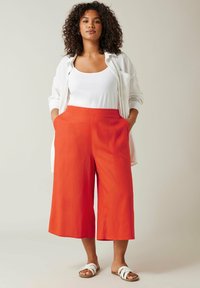 Culottes en lin rouges avec un design à jambes larges, poches latérales, associées à un débardeur blanc et une chemise légère. Comprend des sandales blanches plates.
