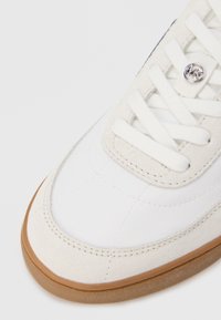 Valge toss, millel on sile sünteetiline pealne ja beežid seemisnahast detailid, ümmarguse kummi tallaga ning hõbedane logodetail keelega.