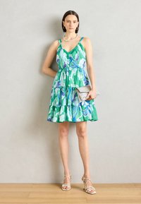 Robe sans manches à imprimé floral en vert et bleu, design à volants superposés avec des volants à l'ourlet. Associée à une pochette argentée et des sandales à talons.