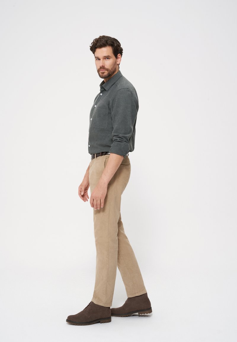 Szara koszula z długim rękawem, beżowe spodnie i brązowe zamszowe buty. Koszula ma kieszeń na piersi, a spodnie mają dopasowany krój z teksturowym wykończeniem.