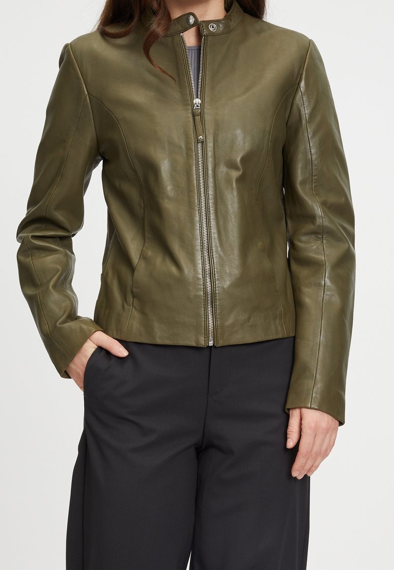 Olivgrön läderjacka med hög krage, dragkedja framtill och figursydd design, med en slät yta och subtila sömdetaljer.