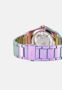 Montre en métal avec un bracelet en acier inoxydable de couleur arc-en-ciel, dotée d'une finition polie et d'un fermoir gravé "GUESS". Boîtier rond en argent visible.