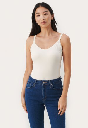 Kermanvärinen tank top ohuiden hihnojen ja V-pääntiöllä, yhdistettynä tiukkoihin tummansinisiin farkkuihin, joissa on nappisuljenta ja etutaskut.