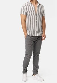 Korte mouwen overhemd in creme met zwarte verticale strepen, gecombineerd met grijze taps toelopende broek en witte sneakers voor een casual look.