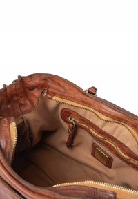 Interno di una borsa a mano in pelle marrone con una fodera in tessuto chiaro, una tasca con zip e un piccolo tag in pelle. Testurizzato, con zip dorate.