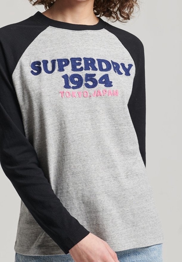Graues und schwarzes Langarm-T-Shirt mit Raglanärmeln. Mit einem navyblauen, gestickten "SUPERDRY 1954" und pinkem "TOKYO, JAPAN"-Text auf der Vorderseite.