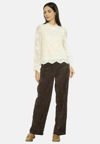 Top in pizzo a maniche lunghe color avorio con motivo floreale e orlo scallop, abbinato a pantaloni a gamba larga in velluto corduroy marrone, completato da scarpe beige.