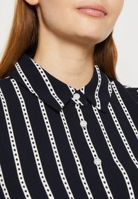 Dunkelblaues Hemd mit Kragen, das dünne weiße Streifen und Rautenmuster aufweist. Verfügt über eine Knopfverschlüsse und eine glatte Stofftextur.